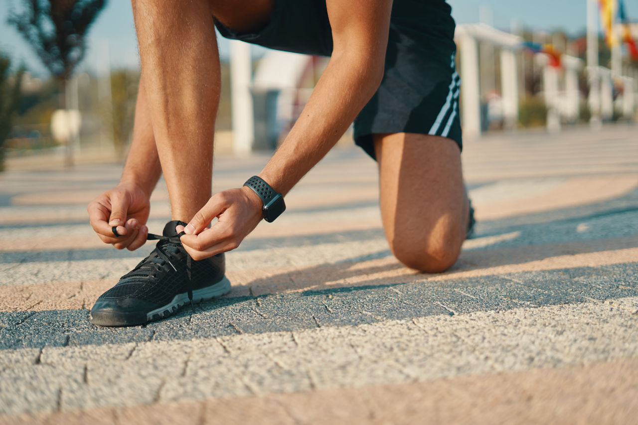 Sportsman ties his black sneakers. Athletic man tying shoelaces while getting ready to run. Smart watch on left hand. Closeup shot