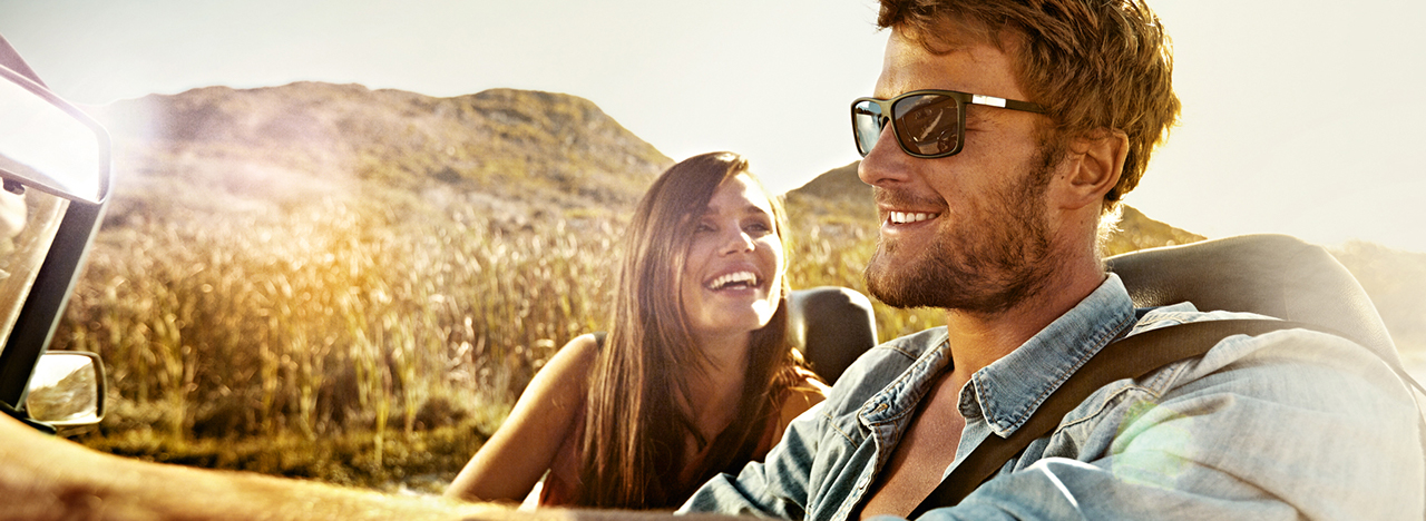 A couple driving in a cabrio in the sun.