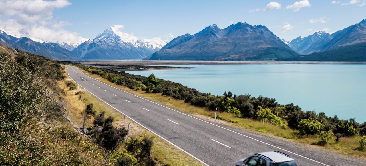 A car on a summer journey next to a lake with mountains in the background.